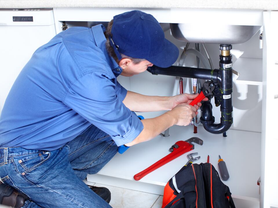 A plumber working on pipes beneath a sink