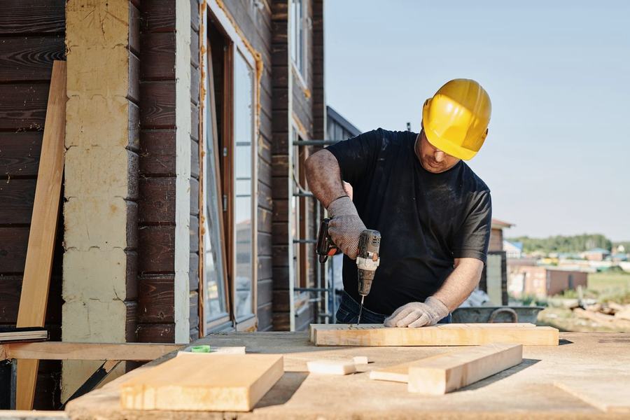 A tradesperson working under a house, hands full, phone out of reach